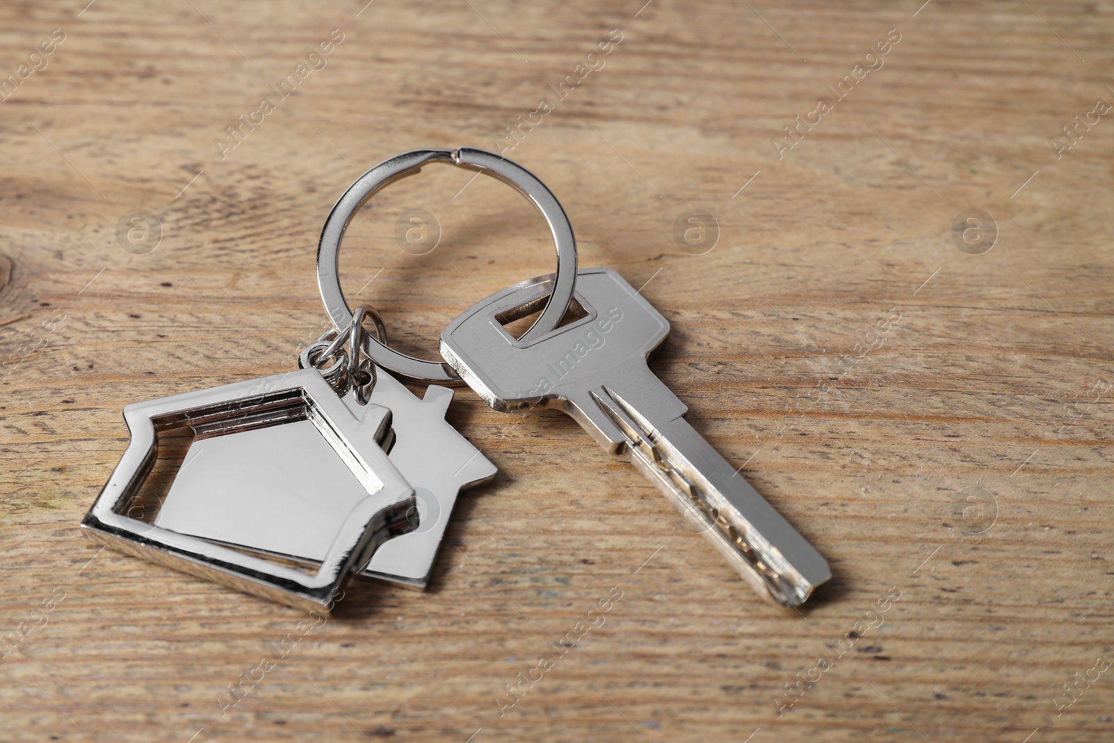 Photo of Key with keychain in shape of house on wooden table, closeup