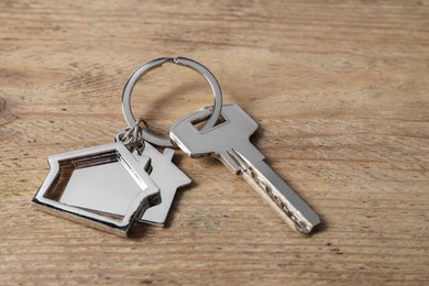 Photo of Key with keychain in shape of house on wooden table, closeup