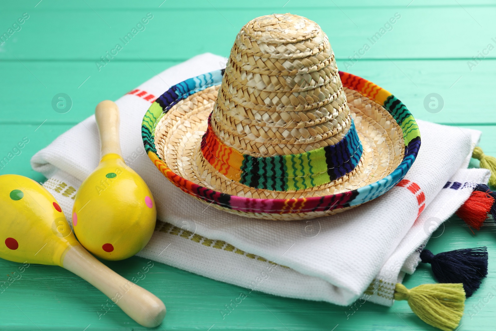 Photo of Mexican sombrero hat, maracas and poncho on turquoise wooden table