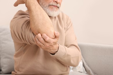 Senior man suffering from pain in his elbow at home, closeup. Arthritis symptoms