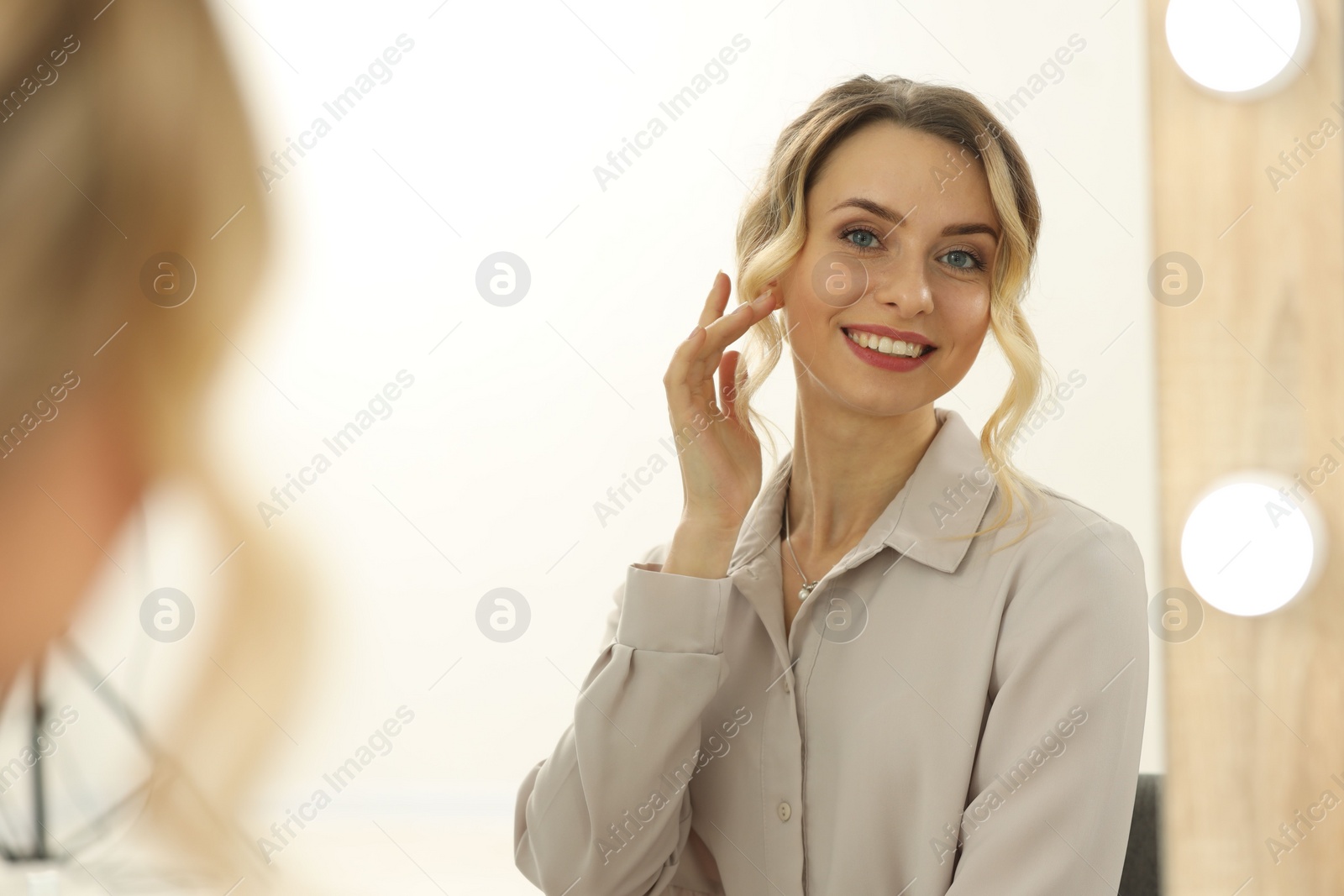 Photo of Smiling woman with beautiful hair style looking at mirror indoors