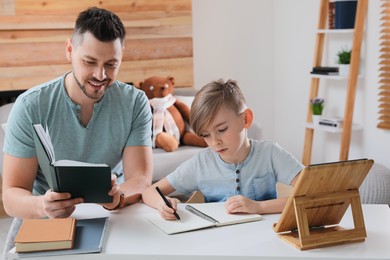 Photo of Boy with father doing homework at table indoors