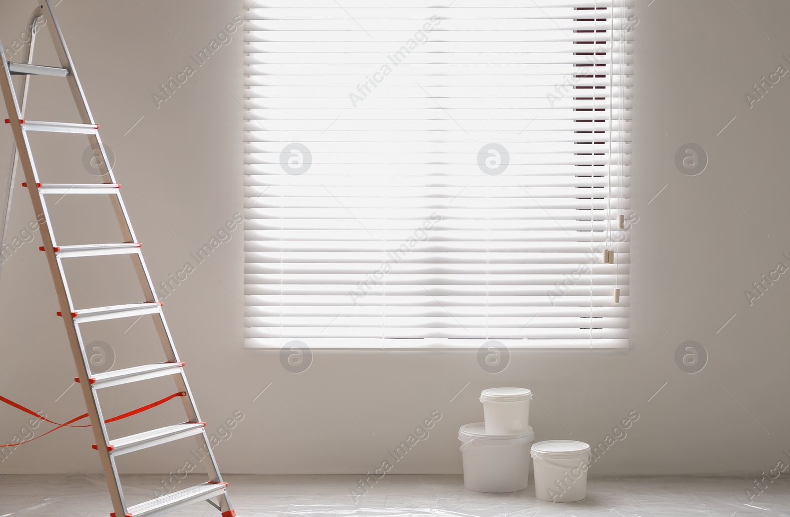 Photo of Stepladder and buckets with paint near wall in room. Interior renovation