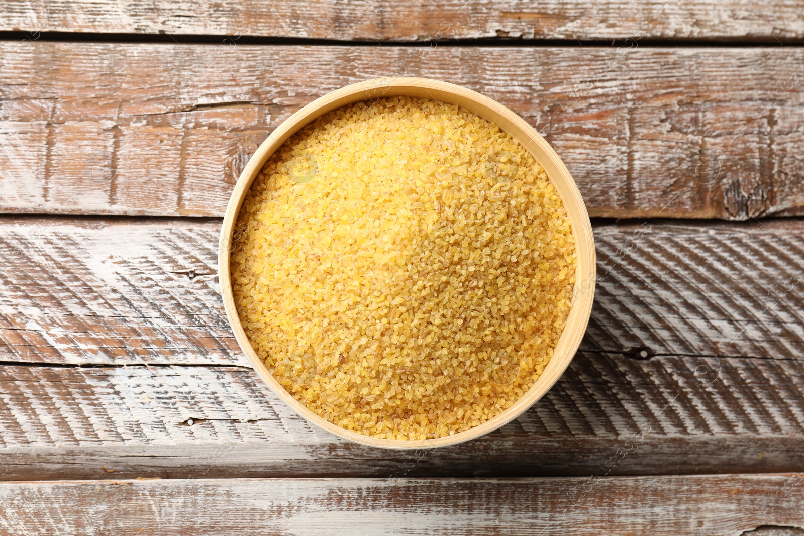 Photo of Raw bulgur in bowl on wooden table, top view