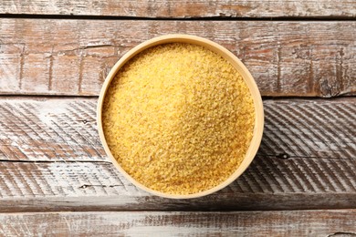 Raw bulgur in bowl on wooden table, top view