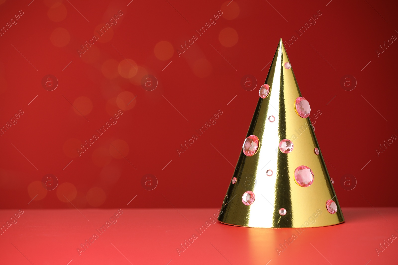 Photo of Shiny golden party hat with rhinestones on red background, space for text