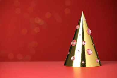 Photo of Shiny golden party hat with rhinestones on red background, space for text