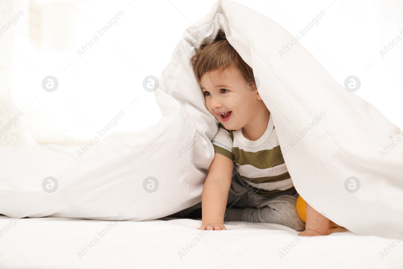 Photo of Cute little child playing under blanket in bed