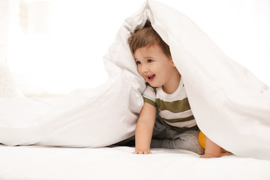 Photo of Cute little child playing under blanket in bed