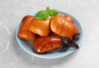 Photo of Delicious baked pirozhki and basil on light grey marble table
