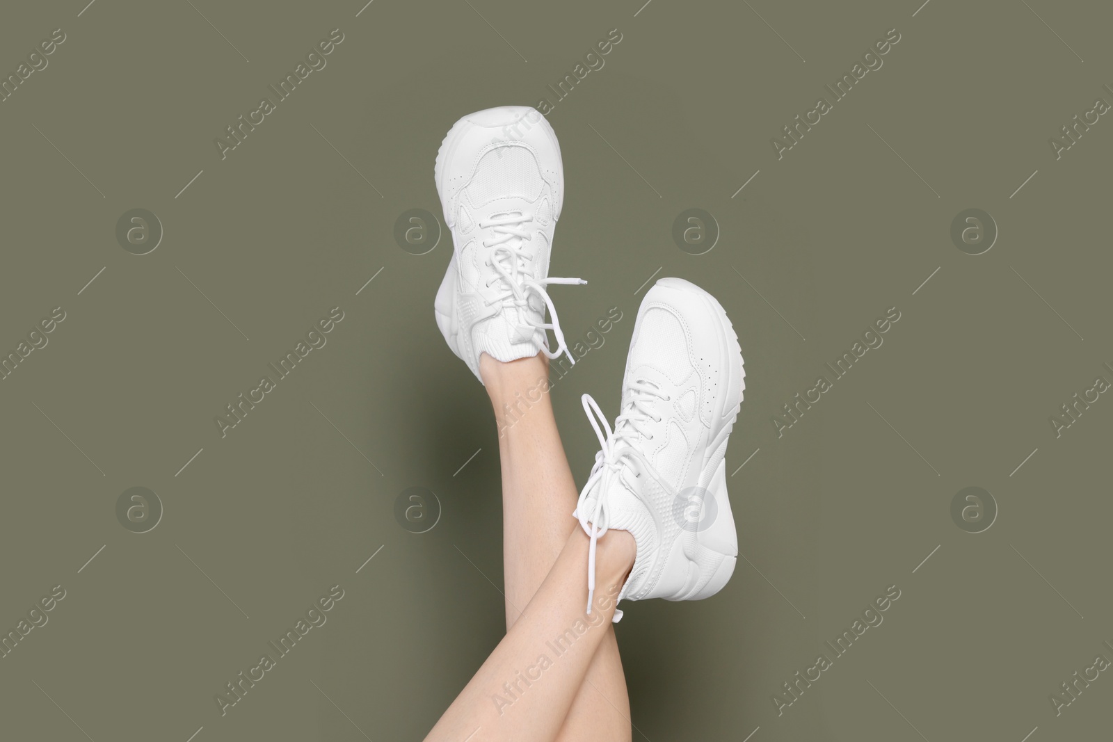 Photo of Woman wearing pair of new stylish sneakers on dark olive background, closeup