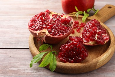 Photo of Fresh pomegranates and green leaves on wooden table, closeup. Space for text