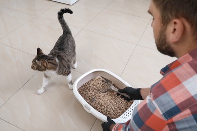 Photo of Young man in gloves cleaning cat litter tray at home