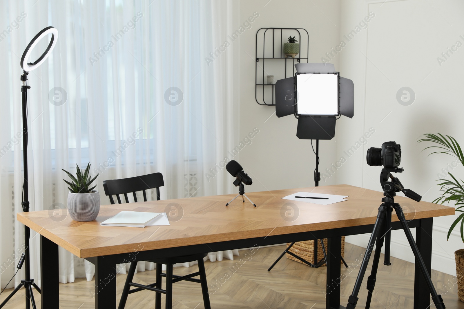 Photo of Camera and lighting equipment on tripods near table in room. Blogger workplace