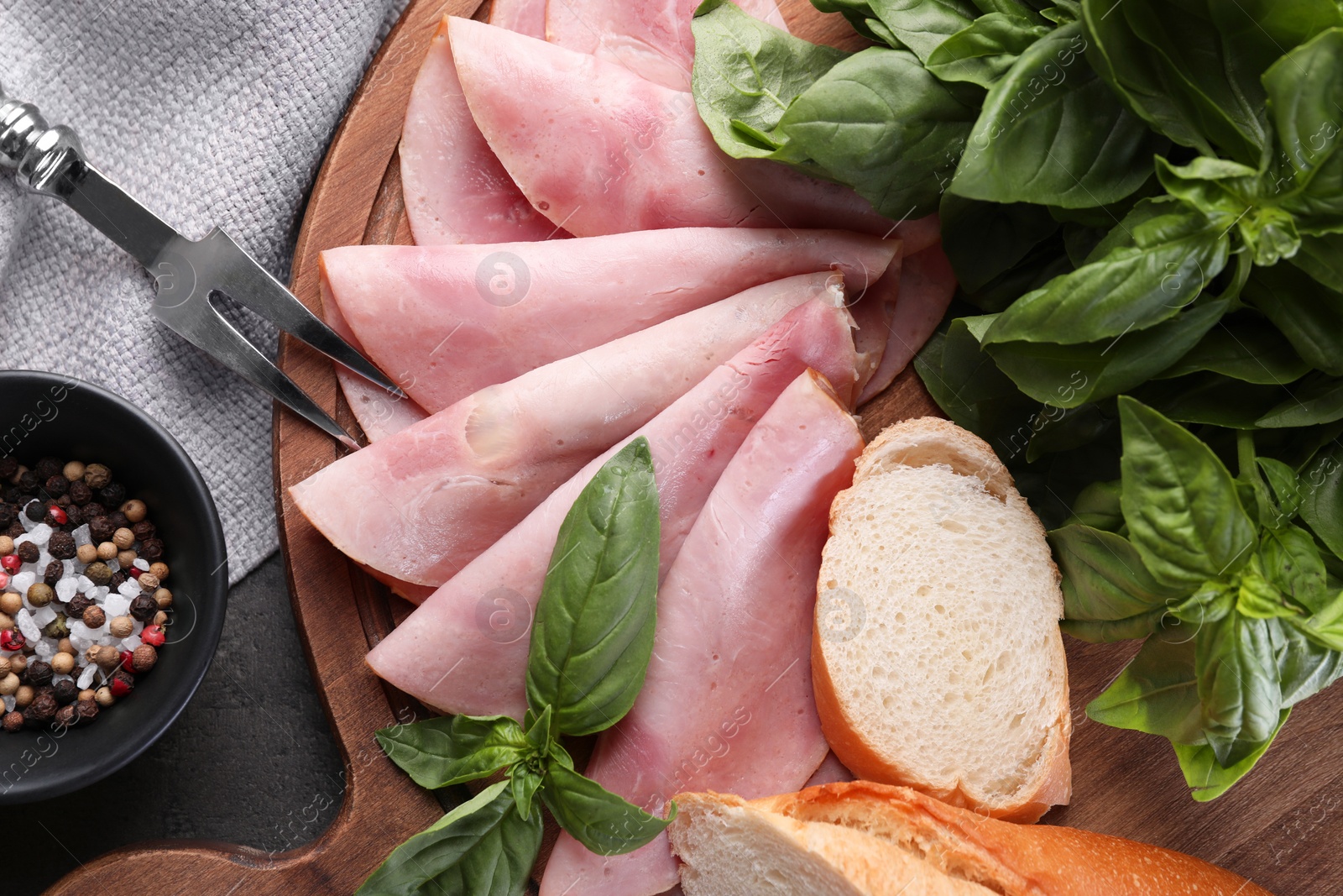 Photo of Tasty ham with basil, bread, spices and carving fork on table, flat lay