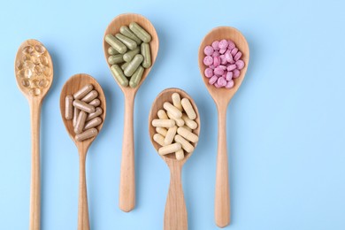 Photo of Different vitamin pills in wooden spoons on light blue background, flat lay