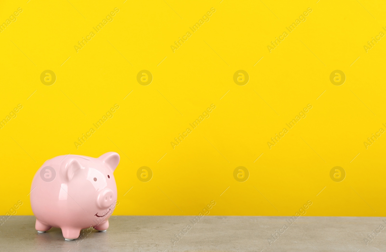 Photo of Pink piggy bank on light grey table against yellow background. Space for text
