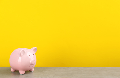 Pink piggy bank on light grey table against yellow background. Space for text