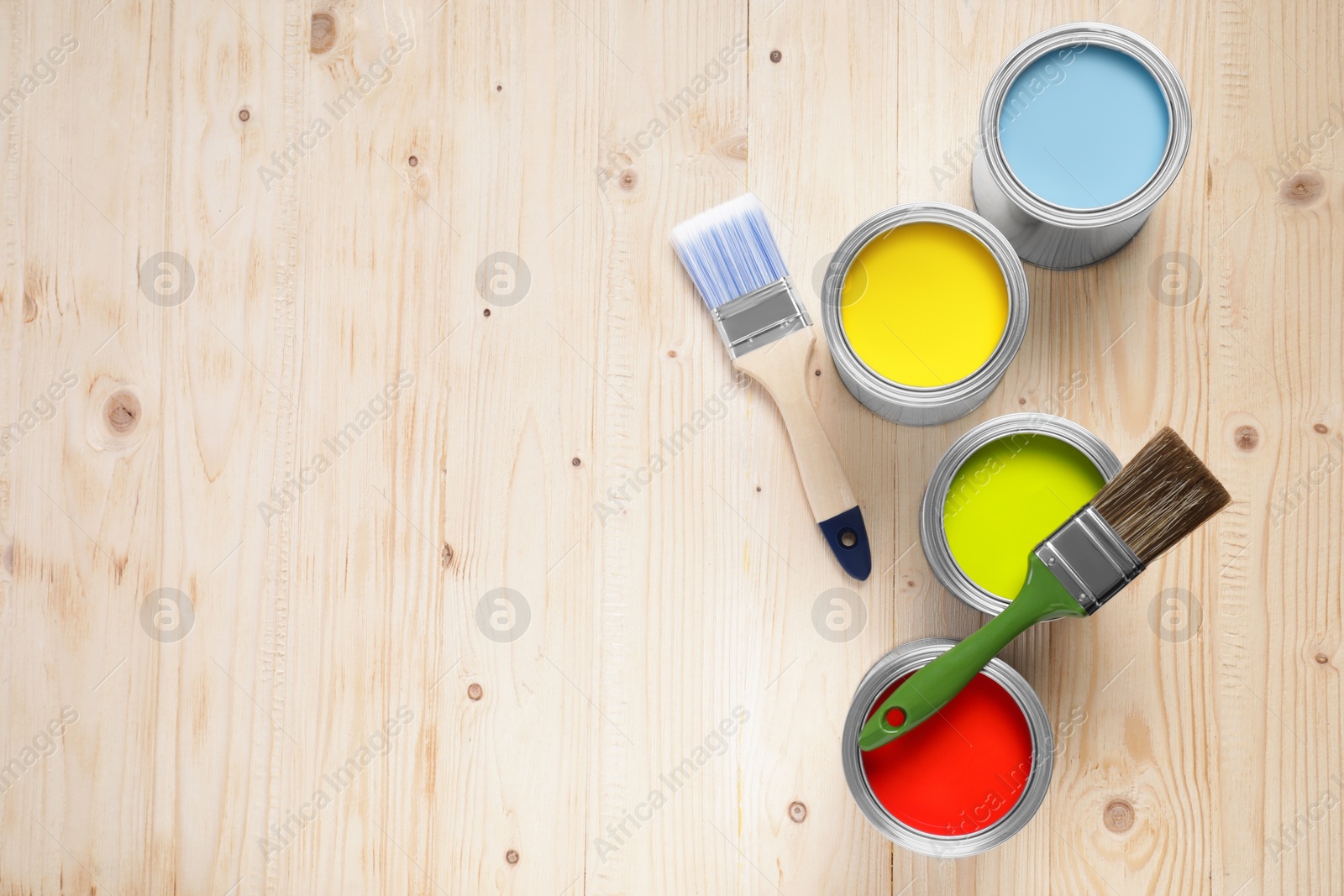 Photo of Cans of different paints and brushes on wooden table, flat lay. Space for text