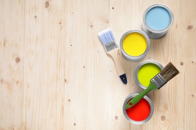 Photo of Cans of different paints and brushes on wooden table, flat lay. Space for text