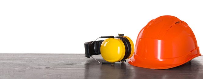 Hard hat and earmuffs on wooden table against white background. Safety equipment