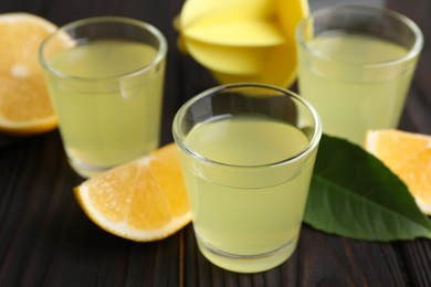 Photo of Tasty limoncello liqueur, lemon and green leaf on dark wooden table, closeup
