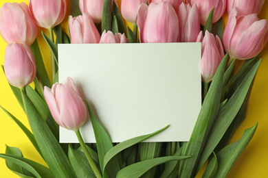 Photo of Beautiful pink spring tulips and blank card on yellow background, closeup. Space for text