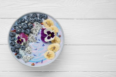 Delicious smoothie bowl with fresh fruits, blueberries and flowers on white wooden table, top view. Space for text