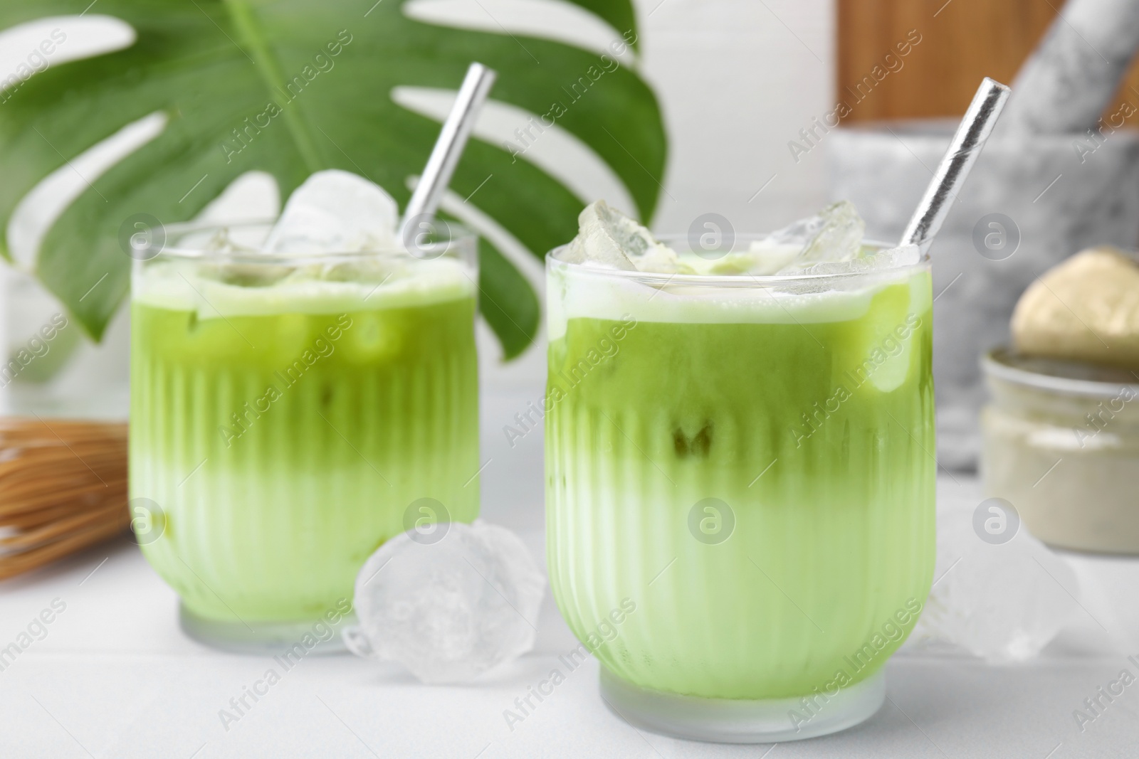 Photo of Glasses of tasty iced matcha latte on white tiled table