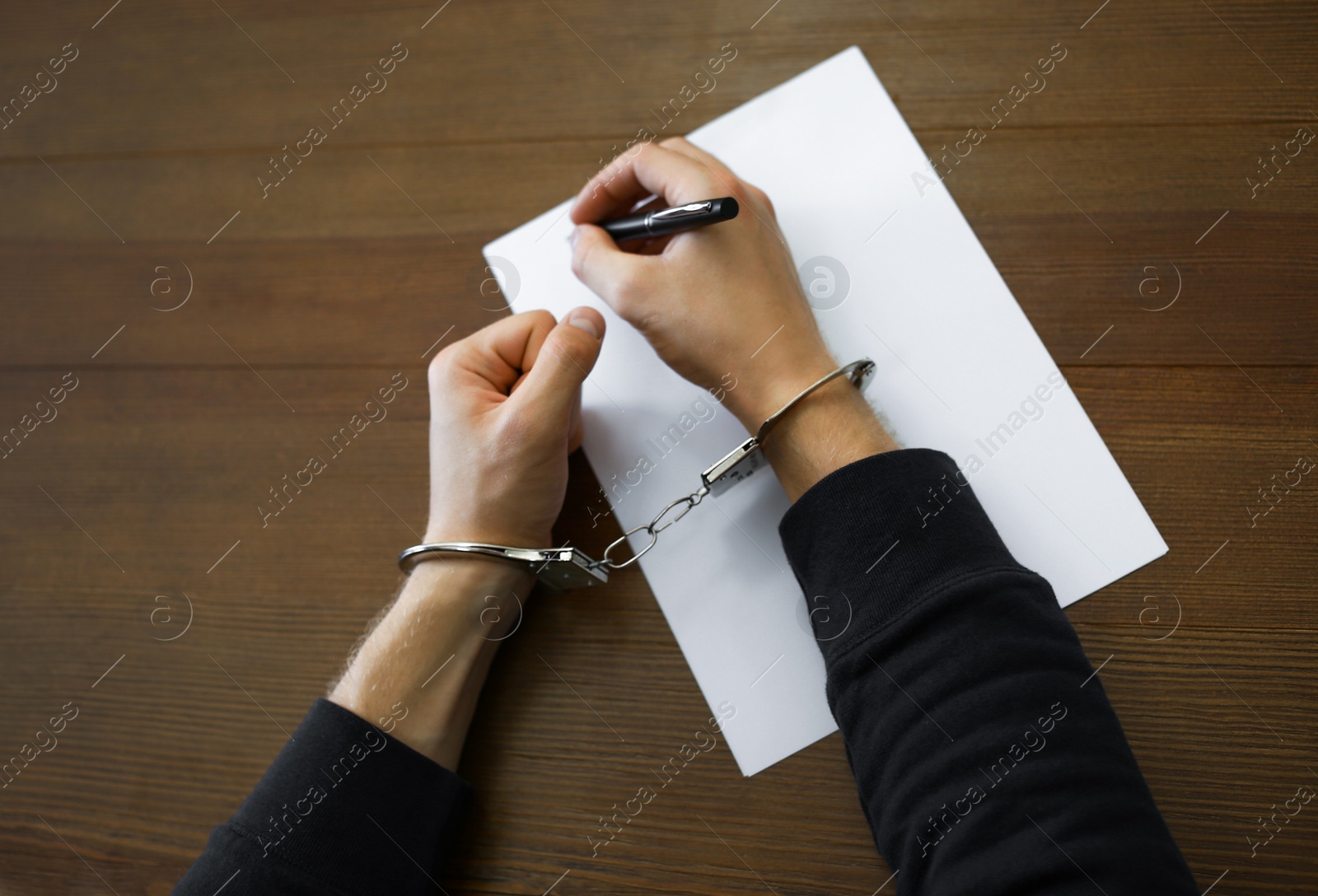 Photo of Criminal in handcuffs writing confession at desk, top view