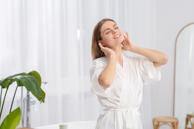 Photo of Beautiful happy woman wearing stylish white robe in light bathroom