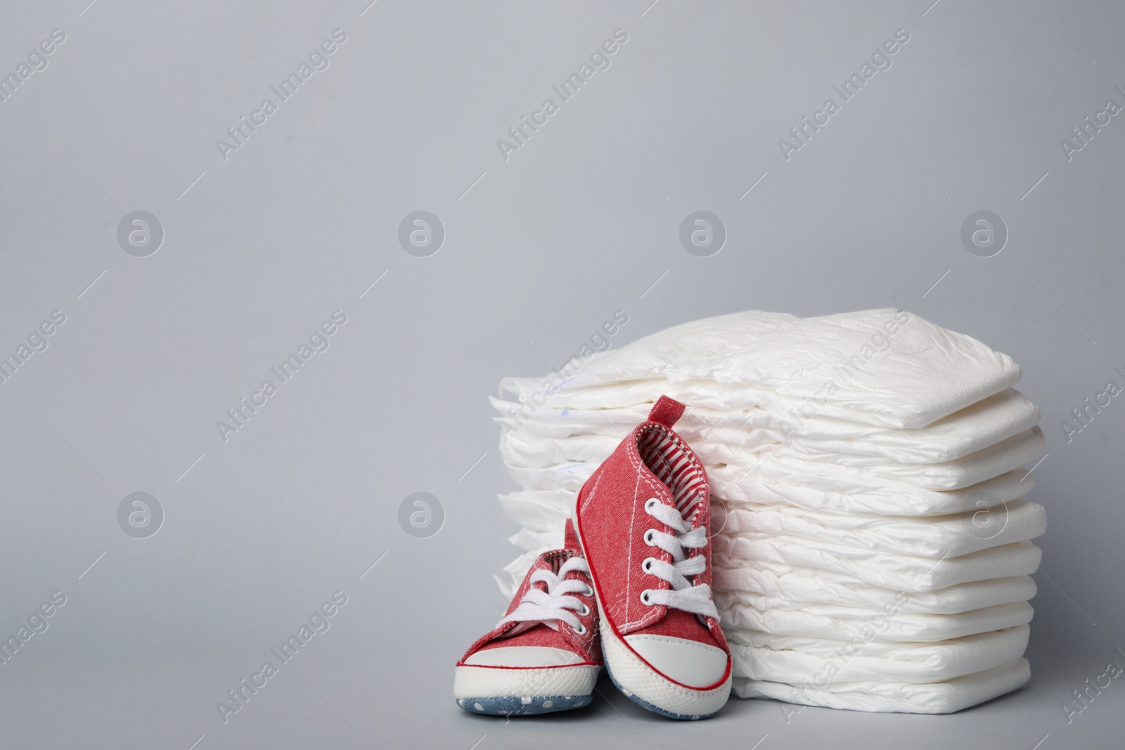 Photo of Diapers and baby shoes on light grey background. Space for text