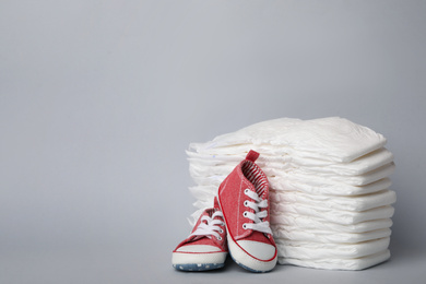Photo of Diapers and baby shoes on light grey background. Space for text