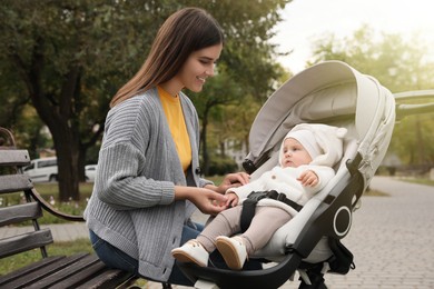 Photo of Happy mother with her adorable baby in stroller sitting on bench outdoors