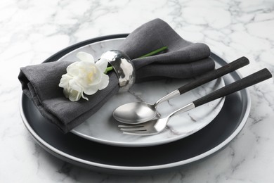 Photo of Stylish setting with cutlery, napkin, flowers and plates on white marble table, closeup