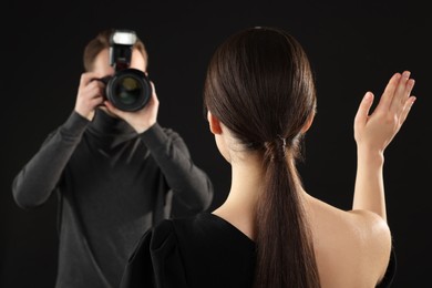 Photo of Photographer taking picture of model on black background, selective focus