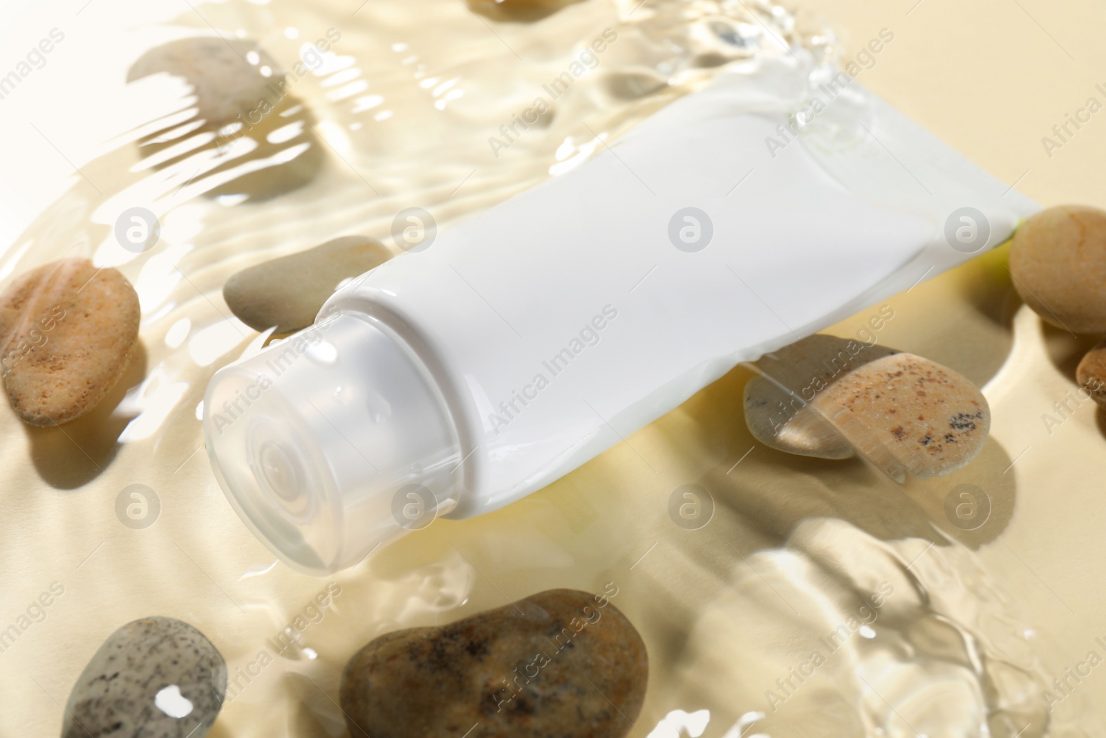 Photo of Tube of face cleansing product and stones in water against beige background, closeup