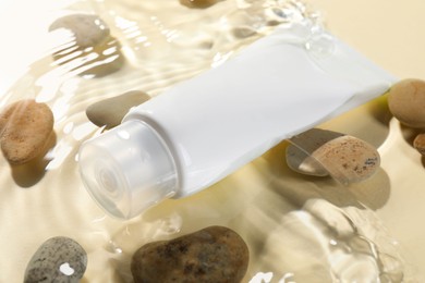 Tube of face cleansing product and stones in water against beige background, closeup