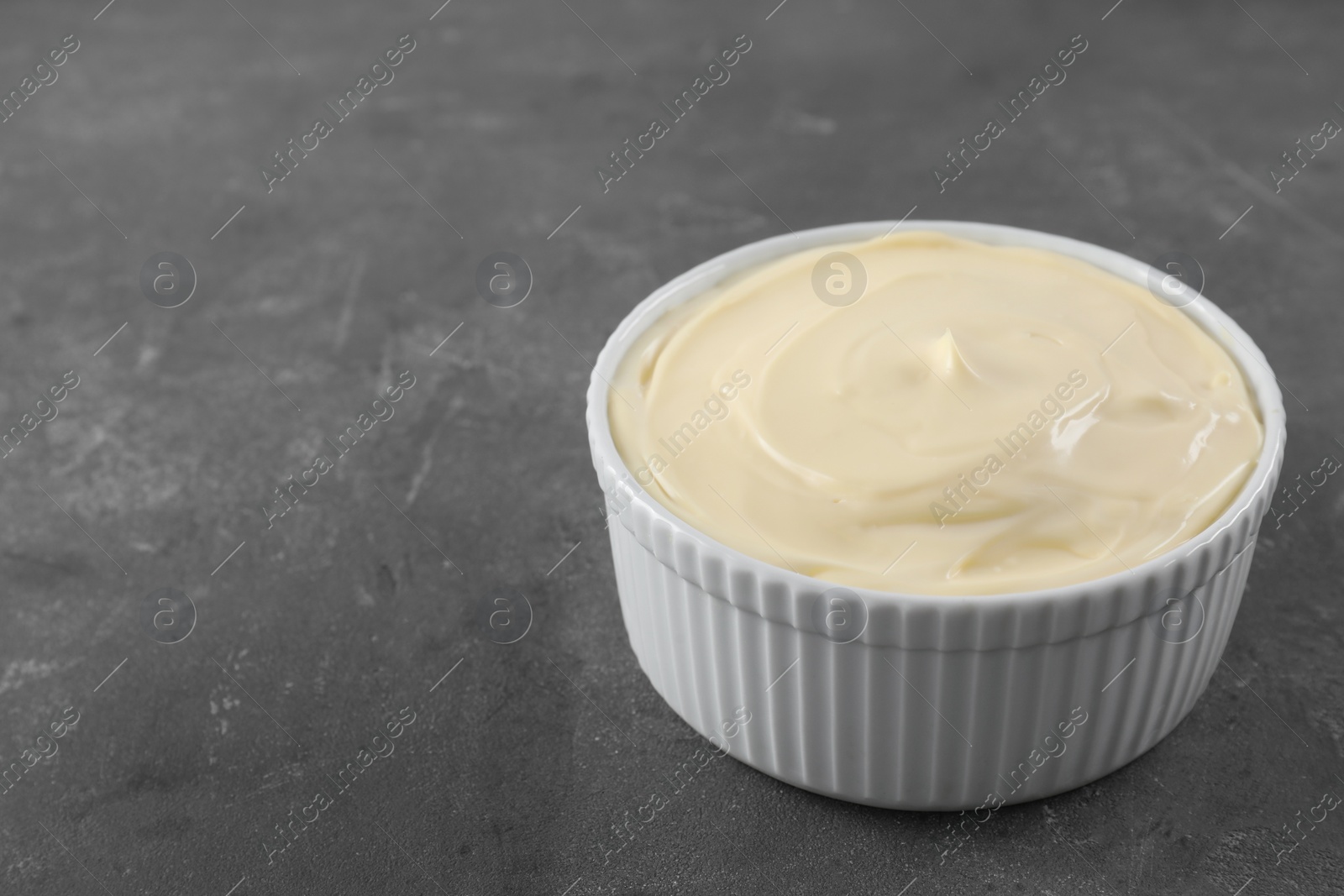 Photo of Fresh mayonnaise sauce in bowl on grey table. Space for text