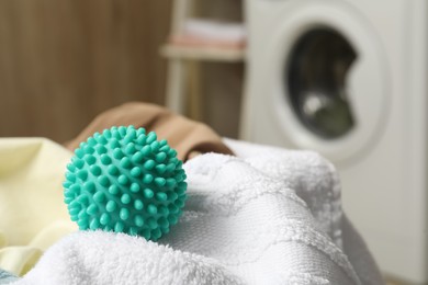 Photo of Turquoise dryer ball and towels near washing machine in laundry room, closeup. Space for text