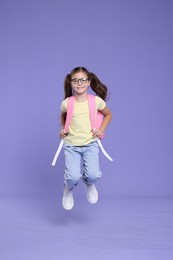 Photo of Cute schoolgirl in glasses with backpack jumping on violet background