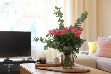 Beautiful bouquet of roses and eucalyptus branches in vase near candles on table at home. Space for text