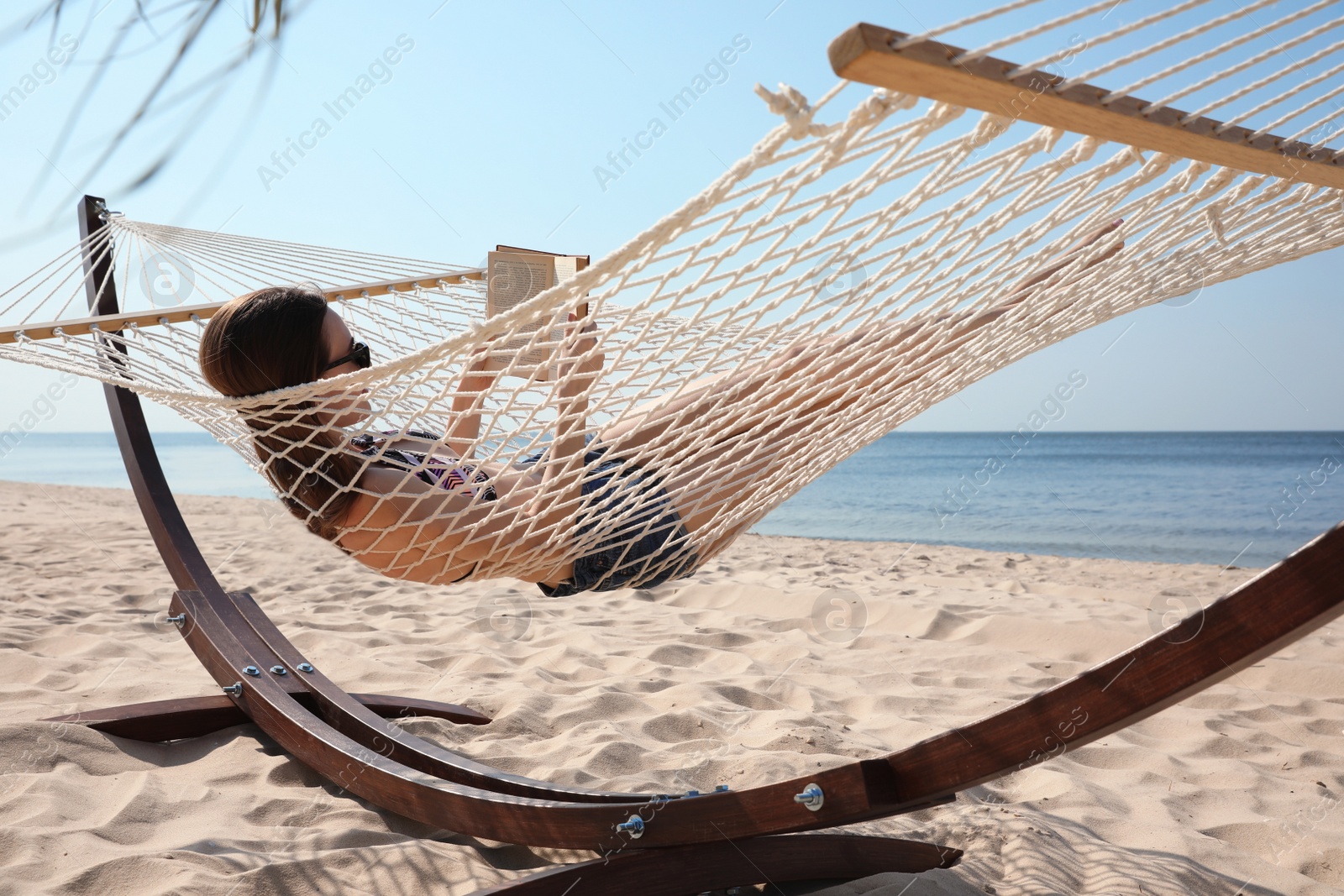 Photo of Young woman reading book in hammock on beach