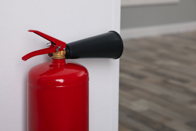 Photo of Fire extinguisher near white wall indoors, closeup. Space for text