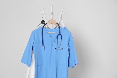 Photo of Medical uniforms and stethoscope hanging on rack against light grey background. Space for text