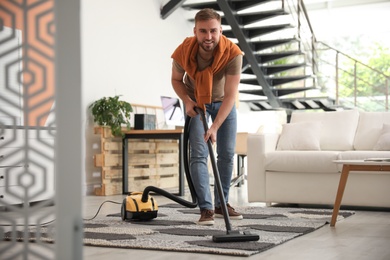 Young man using vacuum cleaner in living room