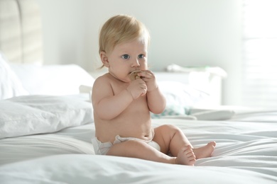 Photo of Cute little baby in diaper with pacifier sitting on bed at home