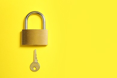 Photo of Steel padlock and key on yellow background, top view. Space for text