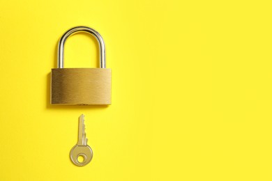 Steel padlock and key on yellow background, top view. Space for text