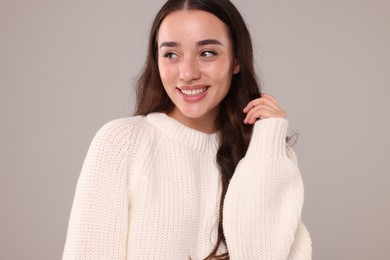 Beautiful young woman in stylish warm sweater on grey background